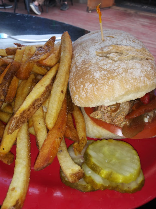 A sandwich with meat and toppings, served with crispy fries and pickles on a red plate.